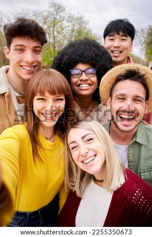 Vertical. Large group of cheerful young friends taking selfie portrait. Happy people looking at camera smiling in outdoor park. Concept of community, youthful lifestyle and friendship in autumn . 