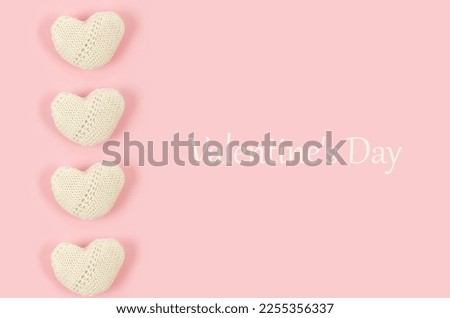 Many white knitted hearts with an inscription "Valentine's day" on pink background. Concept of Valentine day. Greeting card for Valentine. Greeting card with place for text 