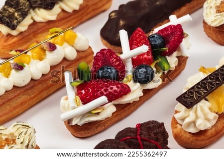 Eclair with berries and meringue. Pavlova eclair. Classic French dessert with delicate mascarpone cream. Nearby are several original eclairs with different flavors. Eclairs on a white background. Royalty-Free Stock Photo #2255362497