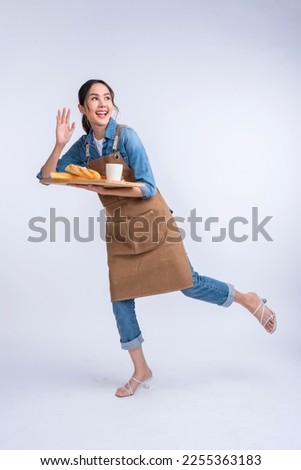 young asian waitress barista wearing apron hand hold bread and coffee drink on wooden tray smiling warm welcome invite customer to her coffee shop studio shot on white background Royalty-Free Stock Photo #2255363183