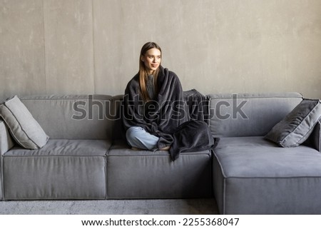 Cute woman relaxing o the sofa wrapped in a soft grey blanket Royalty-Free Stock Photo #2255368047