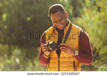 African american guy photographer taking picture with vintage camera on city green park - leisure activity, diversity and hobby concept