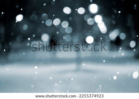 Blurred background. City view, lights, falling snow, night, street, bokeh spots of headlights of moving cars. Diffuse Urban backdrop winter scenery of street in city at night. Lantern light, snowfall