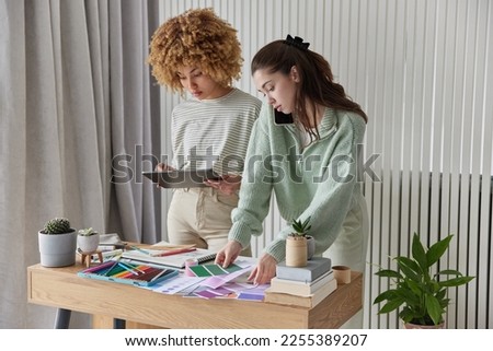 Creative young female designers prepare interiod design plan use modern technologies choose best color on samples call someone stand in coworking space draw sketches. Inspired women architects