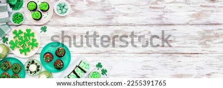 St Patricks Day theme desserts. Corner border against a white wood banner background. Shamrock cookies, green cupcakes, brownies, donuts and sweets. Above view. Copy space.