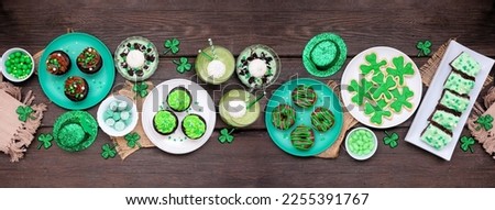 St Patricks Day theme desserts. Table scene over a dark wood banner background. Shamrock cookies, green cupcakes, brownies, donuts and sweets. Top down view.