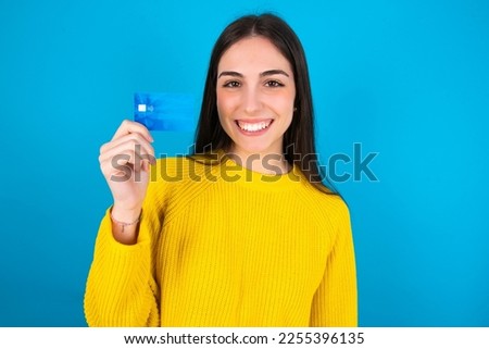 Photo of happy cheerful smiling positive Young caucasian woman wearing yellow sweater over blue background recommend credit card
