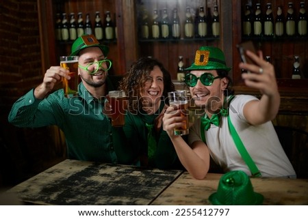 Three friends with beers in a bar for St. Patrick's Day, taking a selfie.