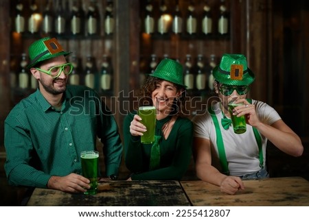 Three friends sharing green beers in a bar for St. Patrick's Day.