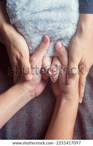 Closeup of parents hands holding newborn baby feet with wedding rings. The concept of the family.. Selective focus Royalty-Free Stock Photo #2255417097