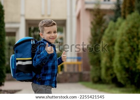 Cheerful mischievous Caucasian schoolboy in blue shirt and school jacket posing showing approval gesture, class. Back to school