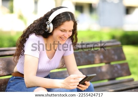 Woman with headphones watching content on smartphone siting on a bench