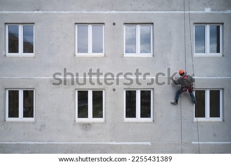 An industrial climber is sealing the joint between the panels on a high-rise facade. Drone footage. Royalty-Free Stock Photo #2255431389