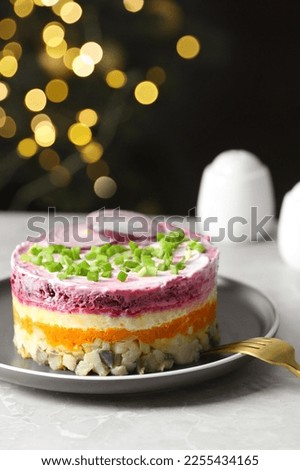 Herring under fur coat salad served on light grey table against blurred festive lights, space for text. Traditional Russian dish