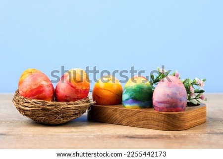 Colorful Easter eggs in a wooden egg stand and a decorative nest of sisal on a blue background with a place for text. Happy Easter concept. Greeting card.