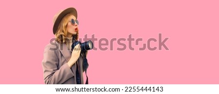 Portrait of stylish happy smiling woman photographer with digital camera taking picture wearing round hat, coat on pink background, blank copy space for advertising text