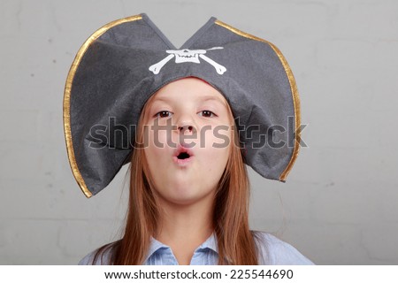 Portrait of a cute cheerful little girl in a pirate hat hamming and makes a funny face on a gray background
