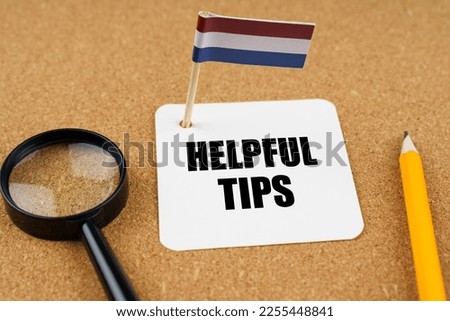 On the table is the flag of the Netherlands, a pencil, a magnifying glass and a sheet of paper with the inscription - Helpful Tips