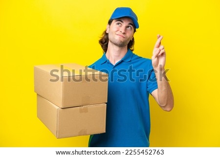 Delivery handsome man isolated on yellow background with fingers crossing and wishing the best
