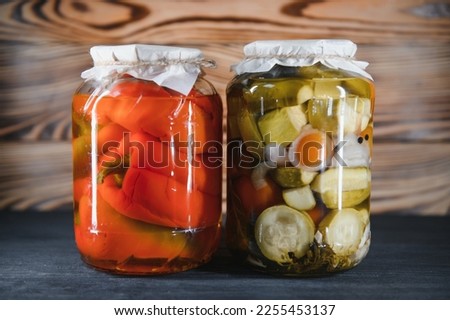Canned cucumbers and tomatoes with craft lids on a wooden background. Cucumbers and tomatoes with place for text. Stocks of canned food. Harvest, stocks for the winter
