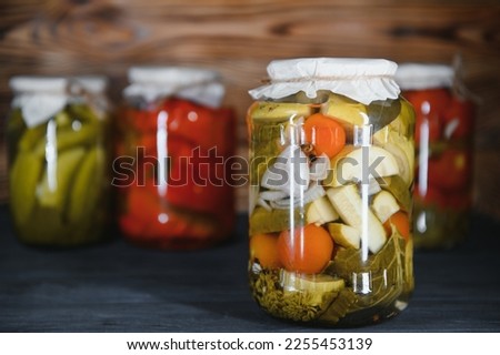 Canned cucumbers and tomatoes with craft lids on a wooden background. Cucumbers and tomatoes with place for text. Stocks of canned food. Harvest, stocks for the winter