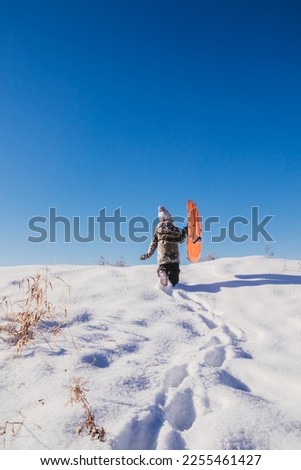 Child carries sled up a hill