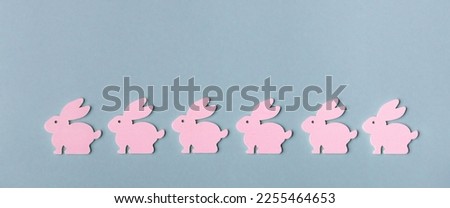 Minimalist creative idea. Six pink Easter bunnies in a line on a blue background. Ornament for Easter card.