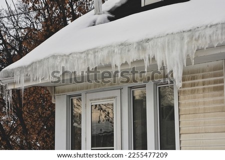 Melting snow on roof creating ice dam in gutter with possible water damage inside. Royalty-Free Stock Photo #2255477209