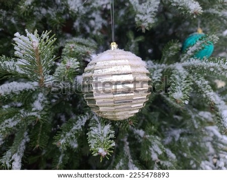 A large Christmas tree ornament hanging on a tree with a bit of snow on it.