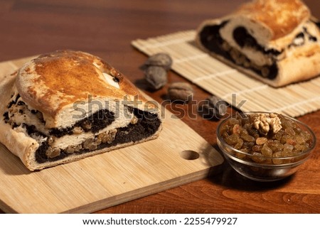 half a baked homemade roll stuffed with poppy seeds and raisins and a glass bowl with raisins and walnuts on a blurred background with half a roll