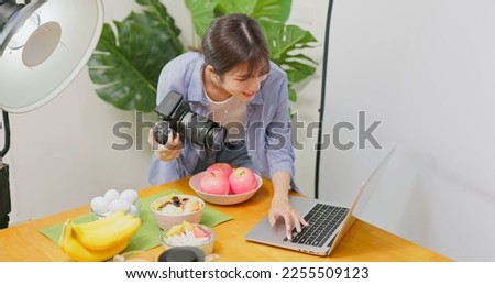 Female Asian photographer taking picture of healthy food checking image with laptop