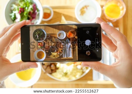 Female hands taking pictures of their breakfast on a mobile phone, top view.