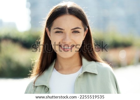 Portrait of gorgeous smiling woman with brunette long hair looking at camera standing in park. Happy fashion model posing for pictures outdoors. Natural beauty concept 