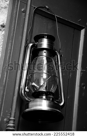 The old kerosene lantern (with dusty glass) hanging on the wooden door of  antique farmhouse. France. Aged photo. Black and white.