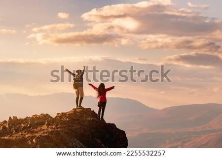 Couple two happy hikers stands with open arms at sunset view point high in mountains