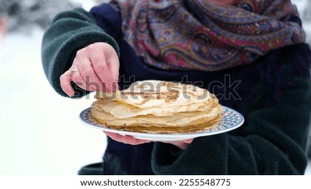 Close-up. A woman holds a plate of pancakes outdoors in winter. Traditional thin Russian pancakes on a plate. Baking for Shrove Tuesday in Russia. Royalty-Free Stock Photo #2255548775