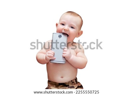 Funny happy baby boy gnaws a phone in his hands. Smiling child holds a smartphone, isolated on a white background