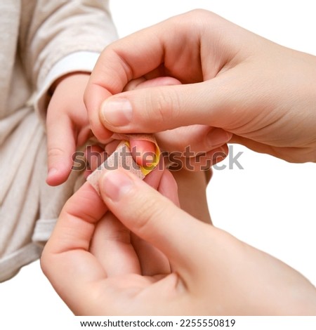 Woman mother sticks a medical band-aid on the toddler baby finger, isolated on a white background. Mom s hand with a sticky wound protection bandage and a child hand