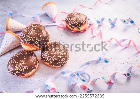 Chocolate Berliner pastry for carnival and party. German Krapfen or donuts with streamers and confetti.  Colorful carnival or birthday image