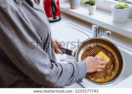 woman's hand washes burnt greasy frying pan with kitchen washcloth in sink. Dirty dishes with burnt food, household chores, washing dishes Royalty-Free Stock Photo #2255577743
