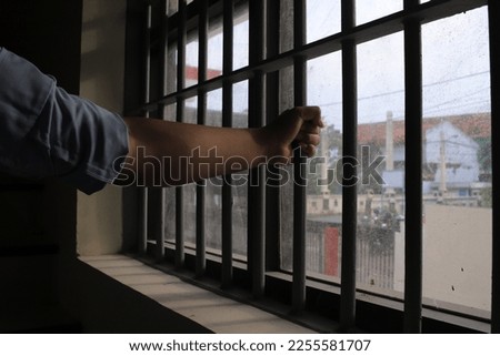 Man in prison hands of behind hold Steel cage jail bars. offender criminal locked in jail. filter dark vintage. Royalty-Free Stock Photo #2255581707