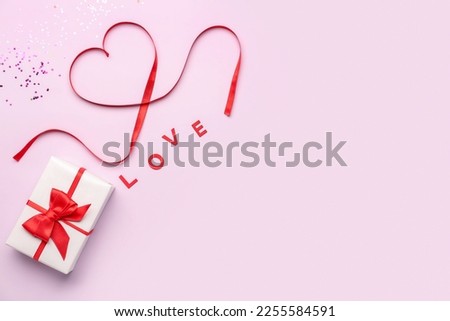 Word LOVE, gift and heart made of red satin ribbon on pink background. Valentine's Day celebration