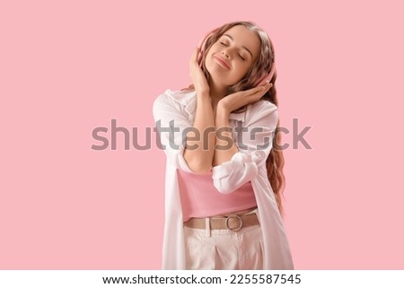 Young woman in headphones listening to music on pink background