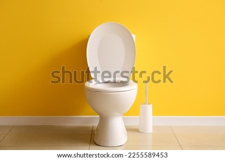 Ceramic toilet bowl and brush near yellow wall Royalty-Free Stock Photo #2255589453