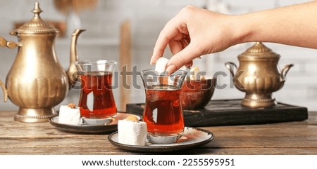 Woman putting sugar cube into cup of Turkish tea on wooden table Royalty-Free Stock Photo #2255595951