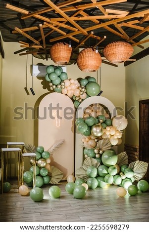 Arch decorated green, brown balloons, neon number one, big paper decor leaves. Birthday party for 1 year old girl or boy on background photo wall. Children's photo zone. Reception at a birthday party. Royalty-Free Stock Photo #2255598279