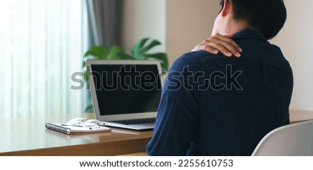 Panorama of young businessman sitting on the desk in the living room at home. He used hands to press down on the shoulder and neck. He is suffering from neck pain from sitting for a long time. Royalty-Free Stock Photo #2255610753