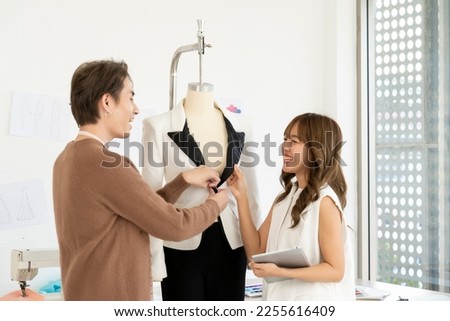Young designer woman use tablet and stylist man is checking beautiful clothes on mannequins for showing product and talking together with happy in fashion studio, copy space Royalty-Free Stock Photo #2255616409