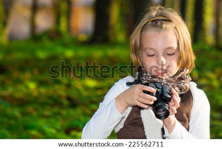 Happy little girl with a camera in autumn park.