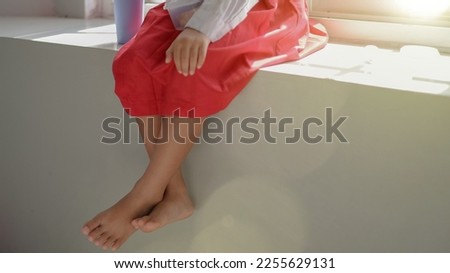 leg of little asian girl sitting on window seat.